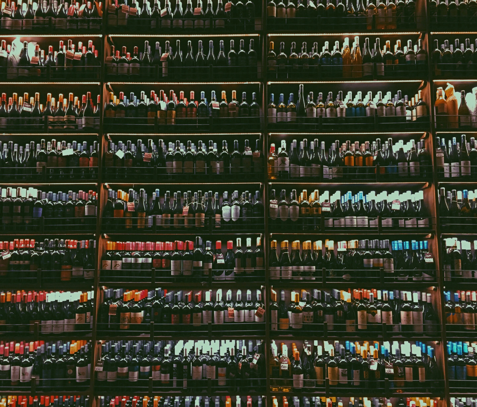 Shelfs with rows of hundreds of wine bottles stocked covering the full photo